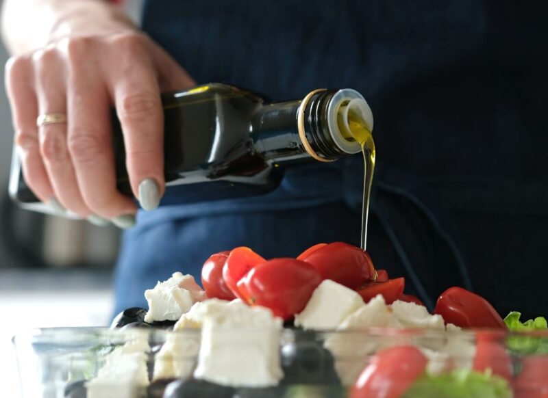 osoba sipa maslinovo ulje preko salate od paradajza, sira, zelene salate i krastavca